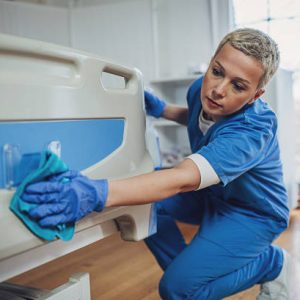 Female nurse cleaning the bed after patients in hospital ward.
